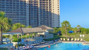 A hotel with a large swimming pool surrounded by lounge chairs and umbrellas, with a tall building in the background. -  Discount option!! Beautiful views! 3BR/3BA Oceanfront condo Ocean Creek Resort! (Myrtle Beach)