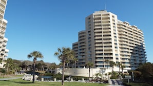 A high-rise hotel with multiple balconies, a landscaped area with palm trees, and a clear blue sky. -  Discount option!! Beautiful views! 3BR/3BA Oceanfront condo Ocean Creek Resort! (Myrtle Beach)