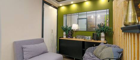 Una sala de estar moderna con un sofá, una butaca, un radiador, un espejo y plantas decorativas.