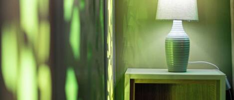 A bedside table with a lamp, a wooden nightstand, and a wall with a greenish tint.