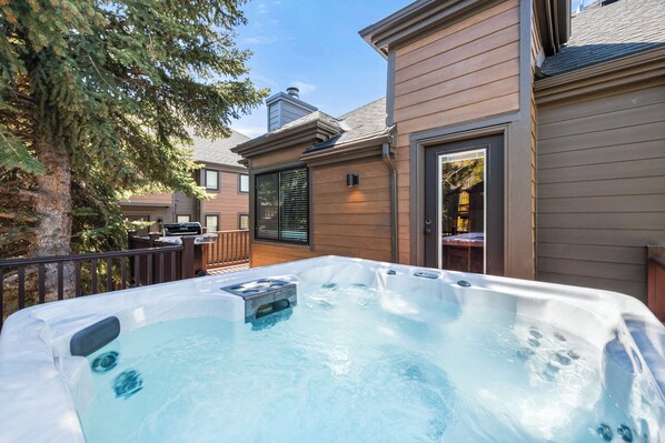 A hot tub on a wooden deck with a house in the background.