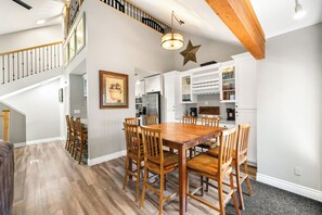 A spacious kitchen with a dining area, wooden chairs, a large wooden table, and a staircase leading to an upper level.