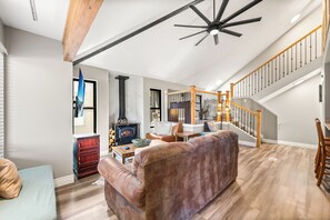 A spacious living room with a fireplace, a staircase, and a large window.