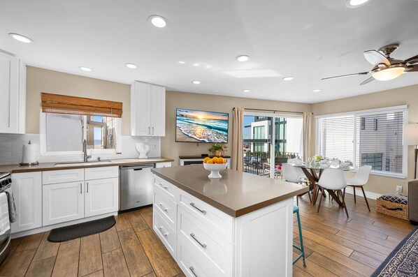 A modern kitchen with white cabinets, a central island, and a dining area with a view of the city.