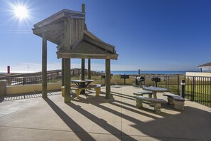 Guests can enjoy the ocean view from shaded picnic tables and benches under a pergola.