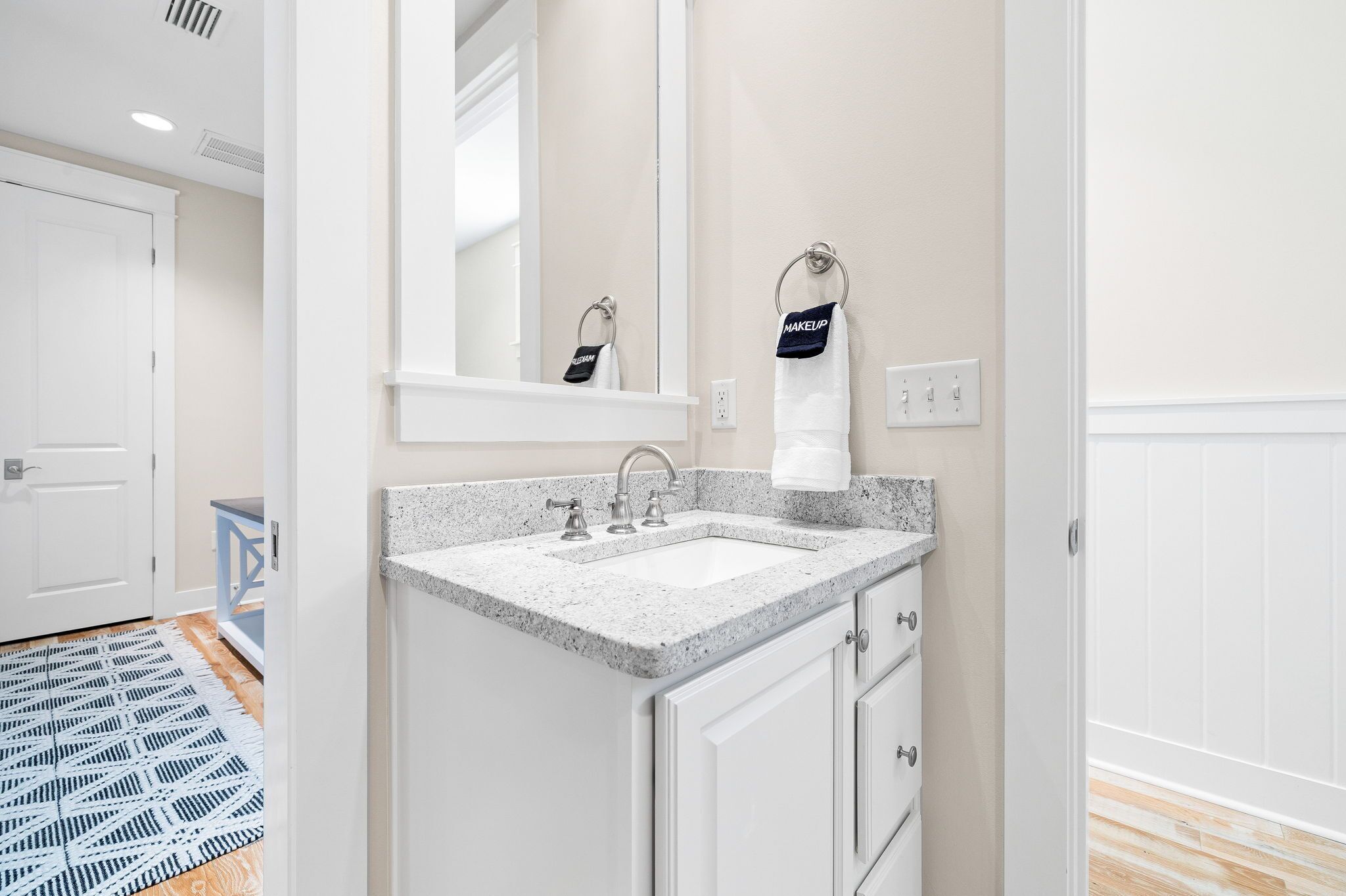 A bathroom with a granite countertop sink, a mirror above it, and a towel rack with a 'Makeup' towel.