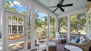 Une véranda avec des fauteuils Adirondack blancs, un canapé en osier et une table.