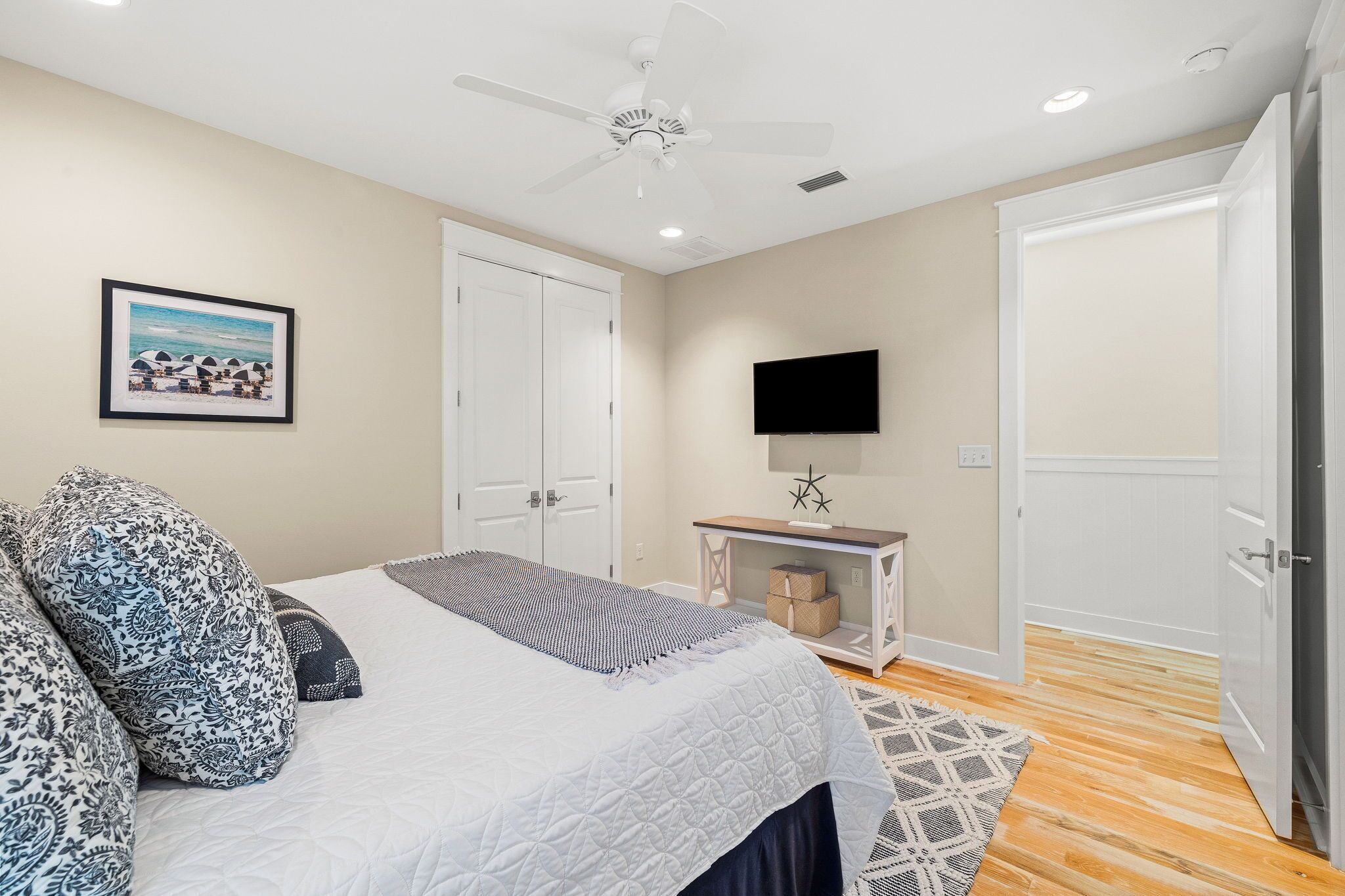 A bedroom with a bed, a ceiling fan, a TV on a stand, and a door.