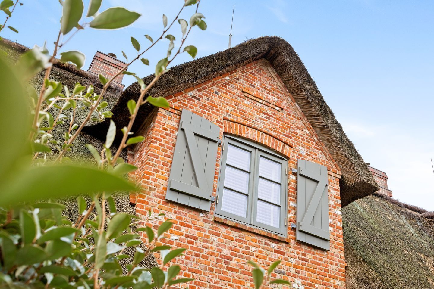 A brick building with a thatched roof and shutters.