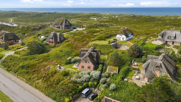 En kustby med traditionella hus som har halmtak, fri utsikt över havet och ett välskött grönområde.