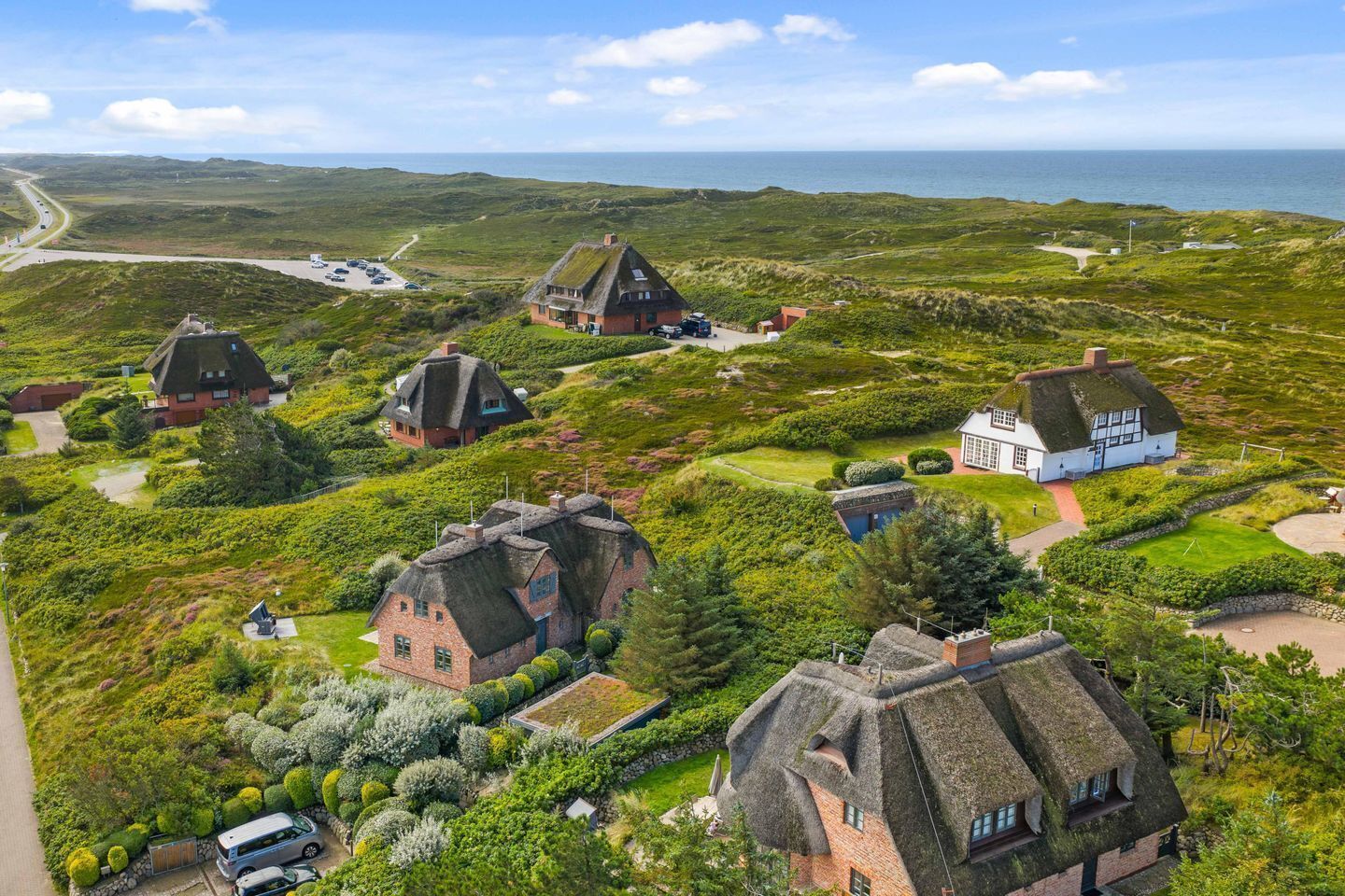 A coastal village with traditional thatched-roof cottages surrounded by lush greenery and a clear view of the sea.