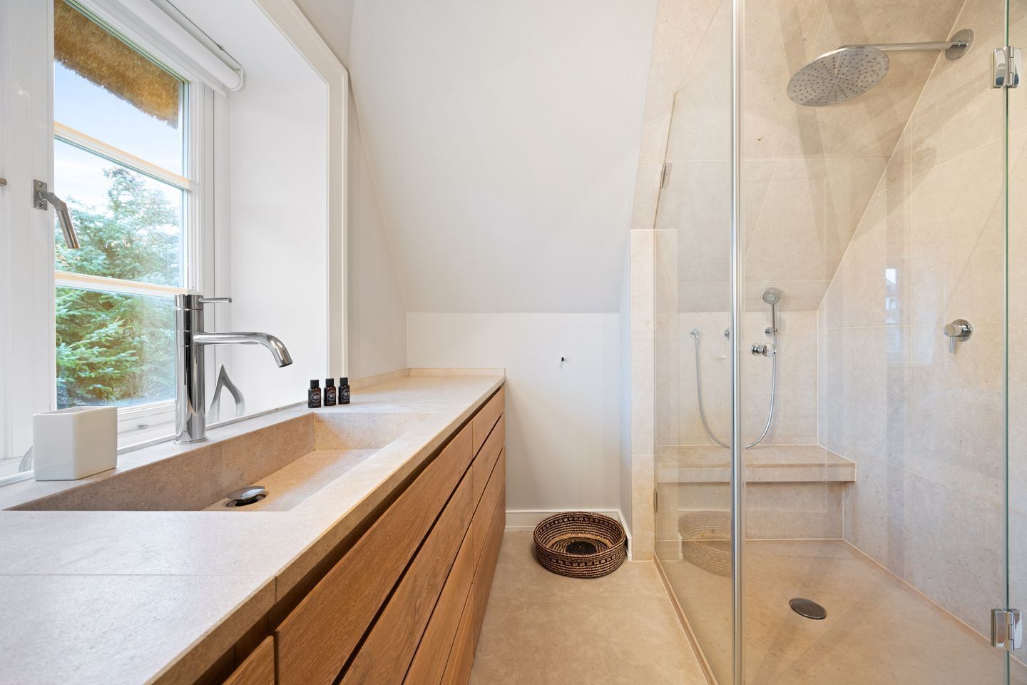 Une salle de bain moderne dotée d’un grand lavabo, d’une douche à parois de verre et d’une fenêtre laissant entrer la lumière naturelle.