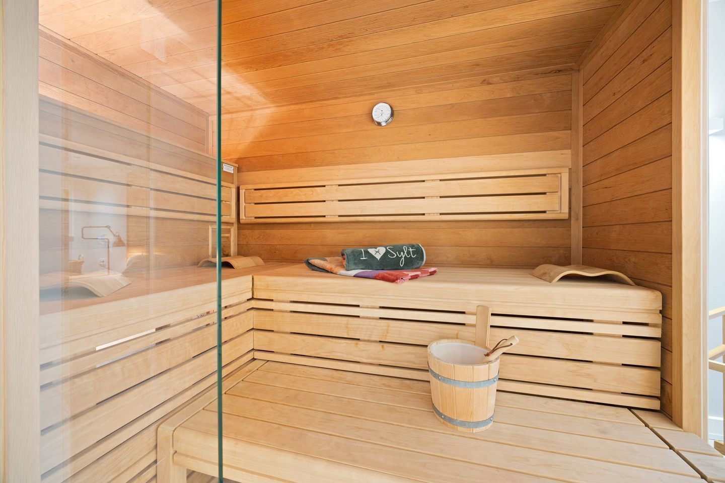 A sauna with wooden benches, a small table with a towel, and a bucket.