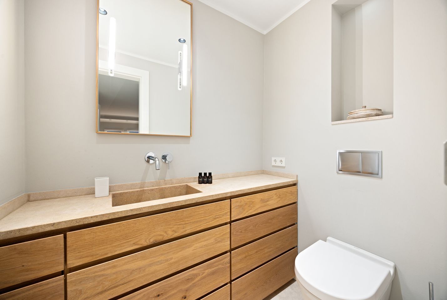 A modern bathroom with a wooden vanity, a large mirror, a white sink, and a toilet.