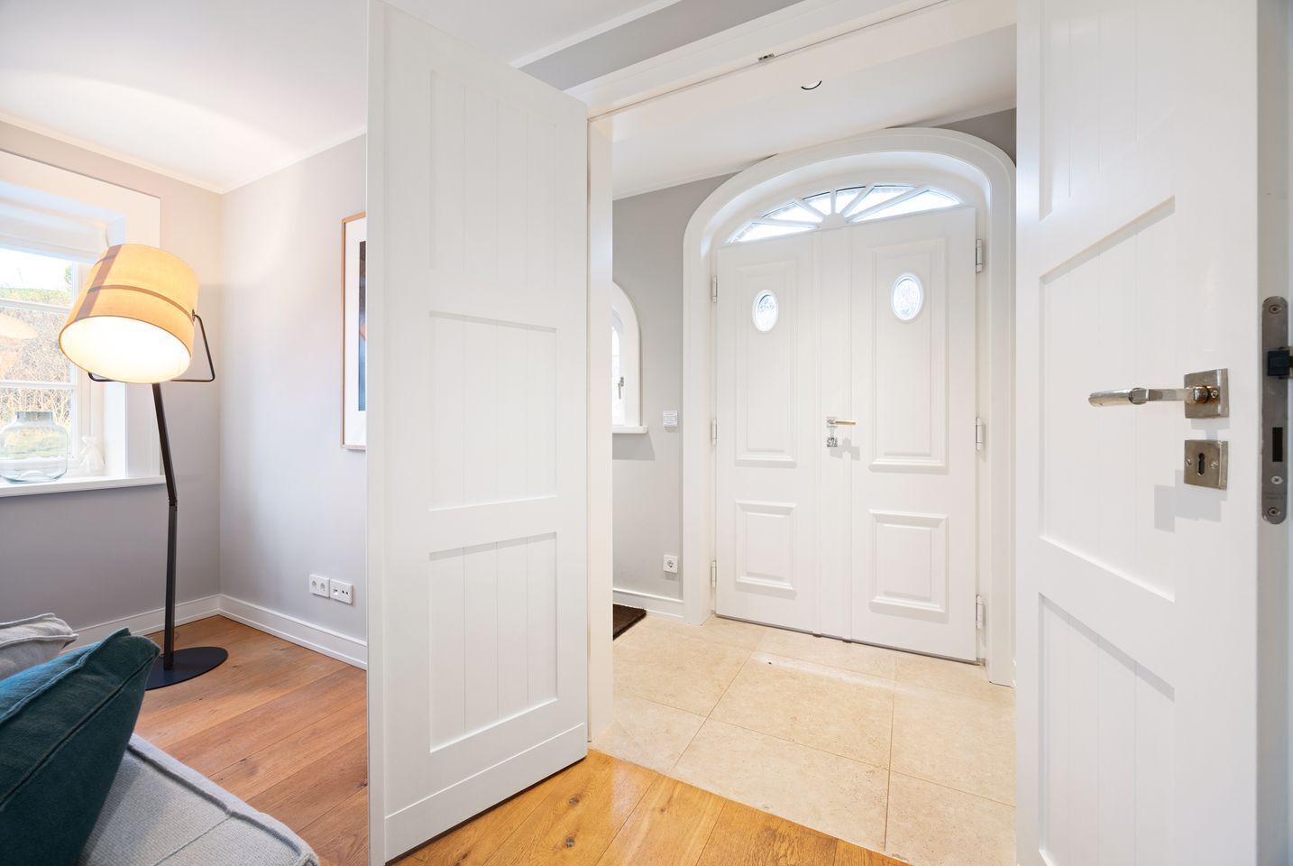 A hallway with white doors, a floor lamp, and a window with a view.