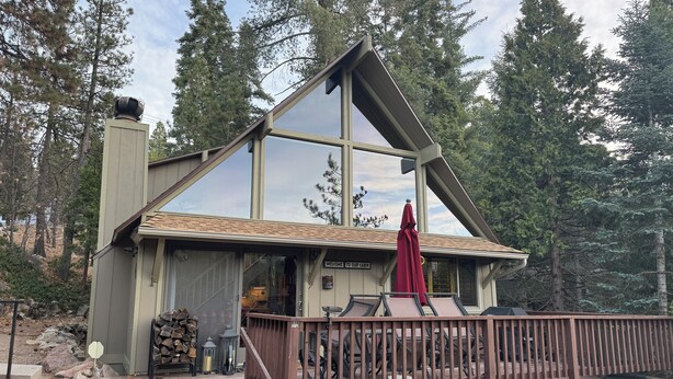 A cabin with a large glass front, a deck with a railing, and a sign that reads "Welcome to Cabin Cabin."
