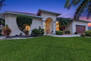 A two-story house with a well-maintained lawn, a large archway entrance, and a garage.