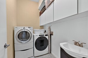A compact laundry room with two front-loading washing machines, a white sink, and a towel rack.