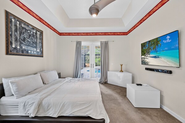 A bedroom with a bed, a painting, a television, and a view of a pool and greenery.