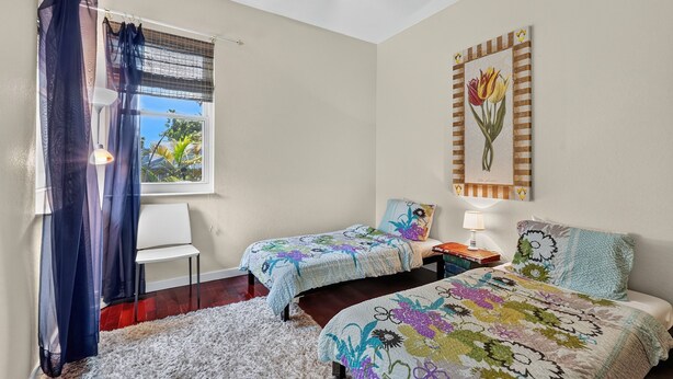 A bedroom with two beds, a window with a view, a ceiling fan, and a wall-mounted artwork. - Luxe Escape in The Forest Country Club - South Fort Myers (Fort Myers)