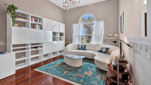 A modern living room with a white sectional sofa, a glass coffee table, and a bookshelf filled with books. - Luxe Escape in The Forest Country Club - South Fort Myers (Fort Myers)