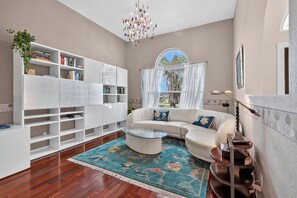 A modern living room with a white sectional sofa, a glass coffee table, and a bookshelf filled with books.