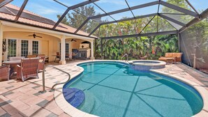 A covered outdoor swimming pool with a patio area, lounge chairs, and a barbecue setup. - Luxe Escape in The Forest Country Club - South Fort Myers (Fort Myers)