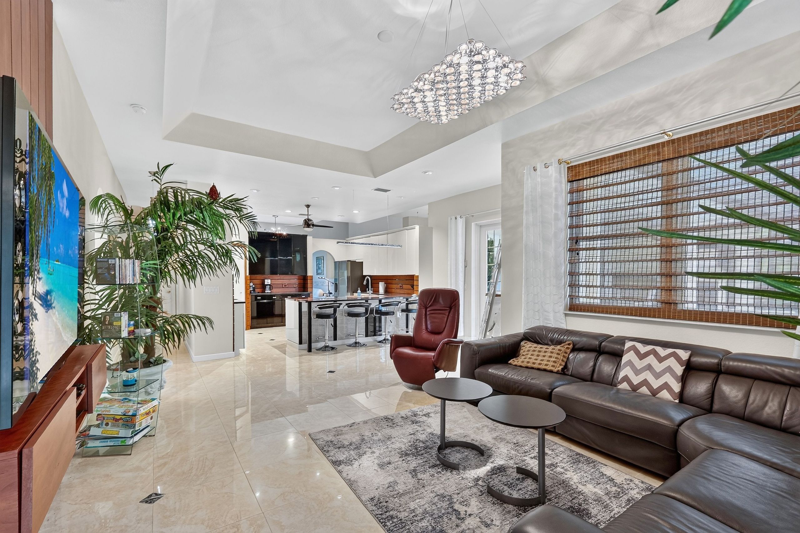 A spacious living area with a modern chandelier, leather sofa, and a large window with a view.