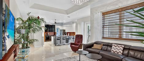 A spacious living area with a modern chandelier, leather sofa, and a large window with a view.