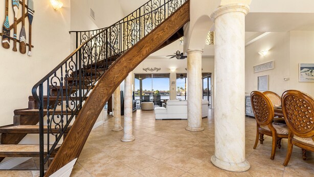 A spacious foyer with a grand staircase, marble columns, and a view of the outdoors.