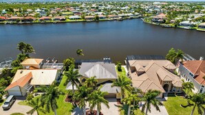 A residential area with houses along a waterfront, featuring a paved driveway and palm trees.