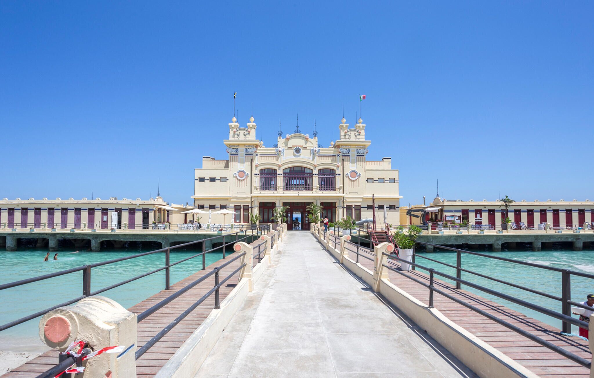 Un hotel frente al mar con una entrada central, varios balcones y vistas despejadas al océano.