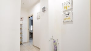 A hallway with a white door leading to a room, a small shelf with books, and two motivational wall art pieces.