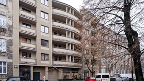 Un immeuble résidentiel à plusieurs étages, doté de balcons, d’un espace de stationnement et d’un arbre aux branches nues.