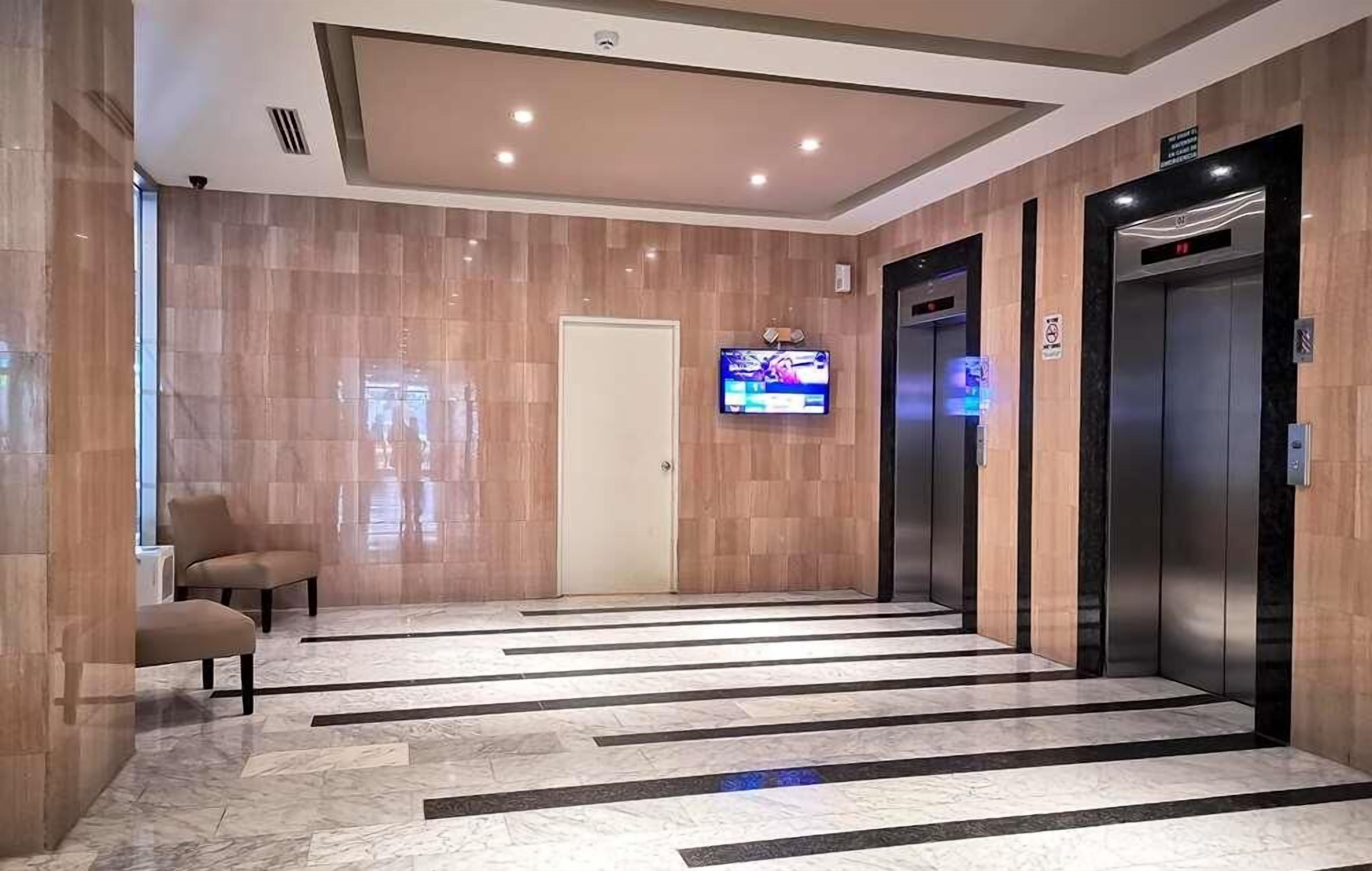 A modern elevator lobby with marble flooring, a television mounted on the wall, and two elevators.