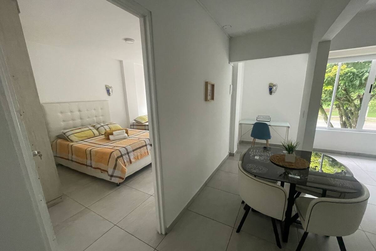 A room with a bed, a dining table with chairs, and a small table with a plant.