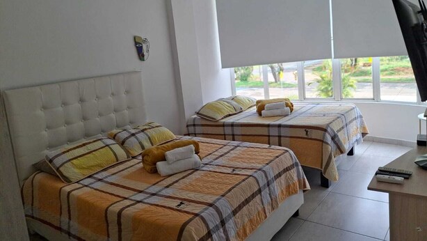 A hotel room with two beds, a desk, and a window with blinds. - Ingenio Park 83 - Apartaestudios (Cali)