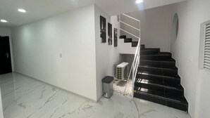 A spacious hallway with a marble floor, a staircase with black steps, and a modern light fixture. - Ingenio Park 83 - Apartaestudios (Cali)