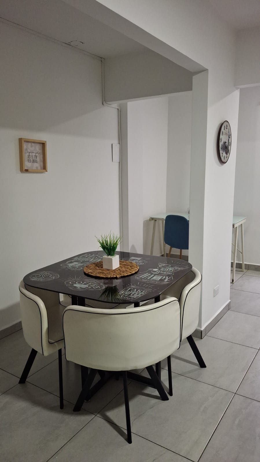 A dining area with a round table, four chairs, a small plant, and a clock on the wall.