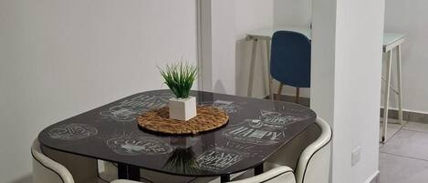 Un comedor con una mesa redonda, cuatro sillas, una planta pequeña y un reloj en la pared.