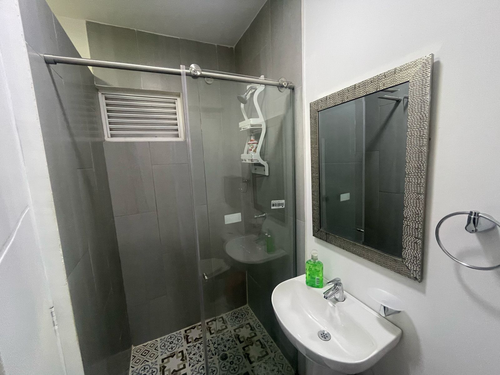 A modern bathroom with a glass-enclosed shower, a white sink, and a mirror with a decorative frame.