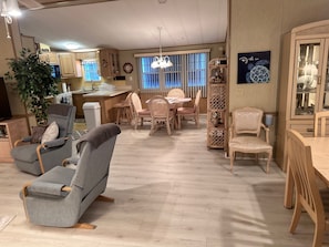 A spacious living area with a dining table, chairs, a sofa, and a kitchen in the background.