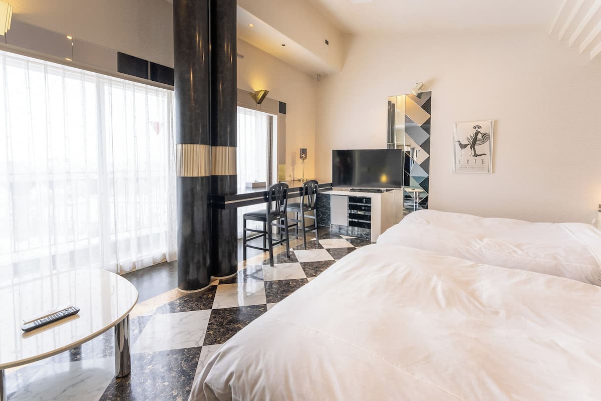 A modern hotel room with a large bed, a desk with a TV, and a dining area.