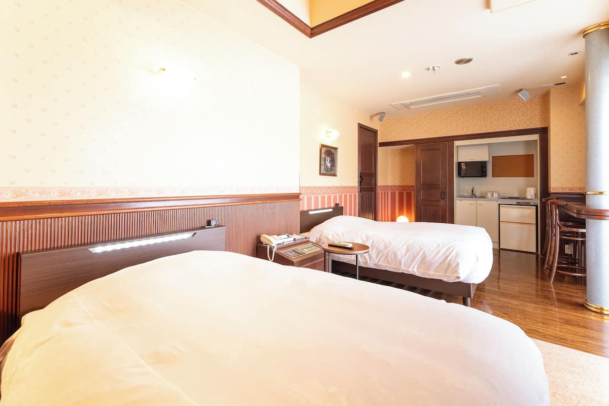 A hotel room with two beds, a small desk, a chair, a microwave, a coffee maker, and a bathroom visible through an open door.