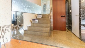 Un escalier moderne, avec une porte en bois en haut, une rampe en verre et un présentoir métallique contenant des sacs.