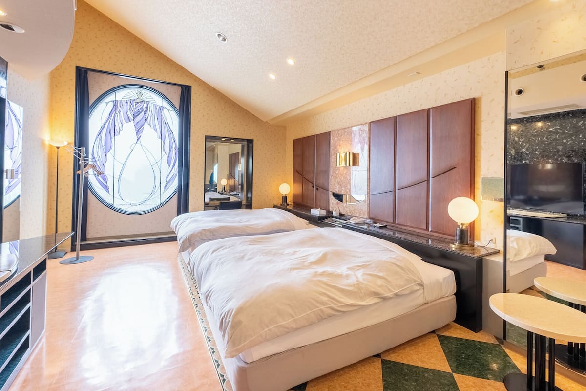 A hotel room with a large bed, a desk with a chair, a TV, and a large mirror.