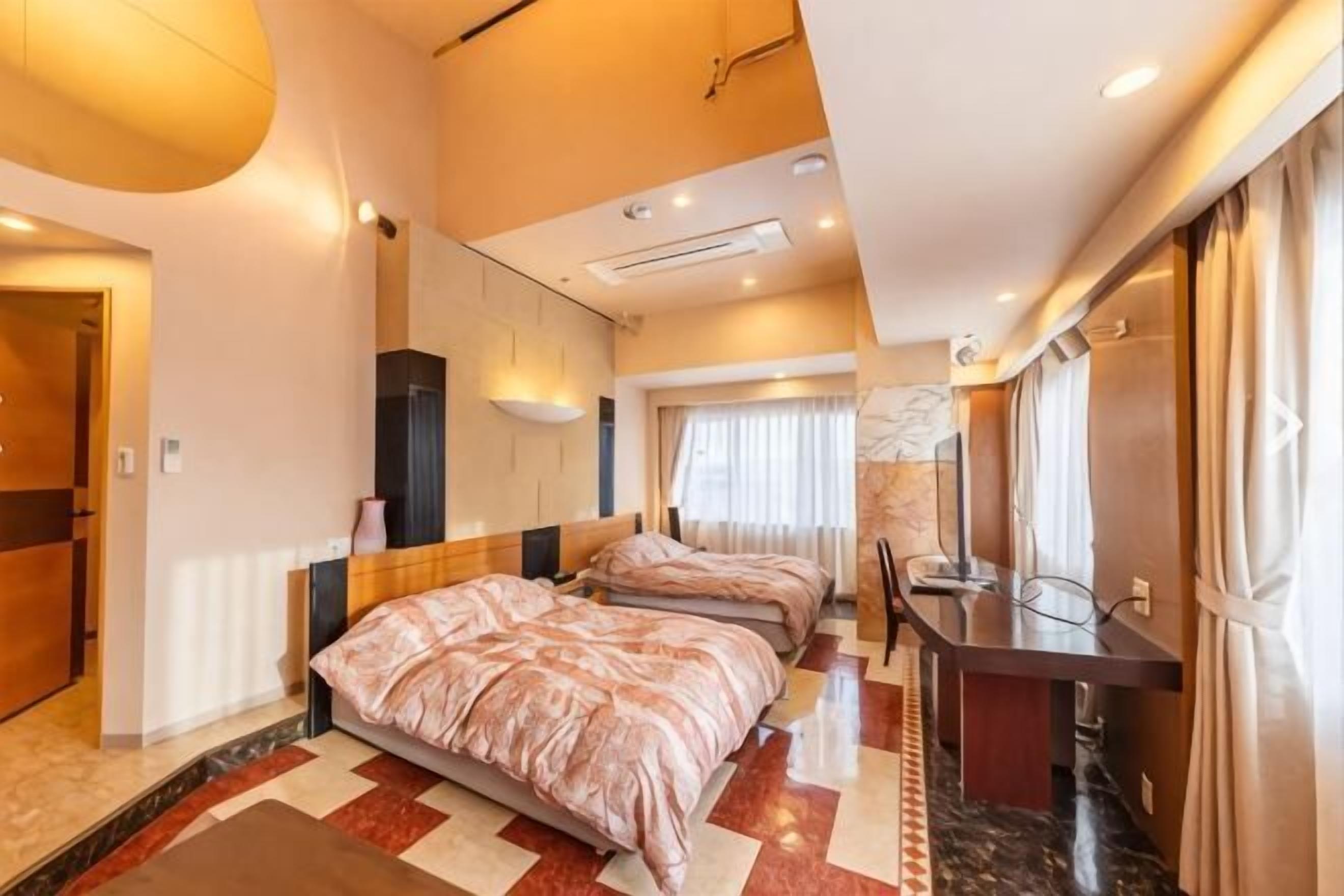A hotel room with two beds, a desk, a mirror, and a large window.