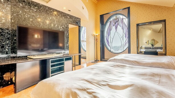 Une chambre d’hôtel dotée d’un grand lit, d’un téléviseur à écran plat posé sur un comptoir en marbre, d’un grand miroir et offrant une vue décorative sur l’extérieur.
