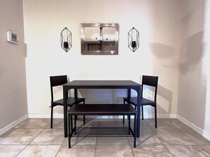 A dining area with a rectangular table and four chairs, two wall-mounted light fixtures, and a built-in light above the table.