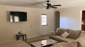 A living room with a beige sofa, a coffee table, a TV, and a ceiling fan. - Desert Voyage | Pool | Near ASU + Old Town Scottsdale (Tempe)
